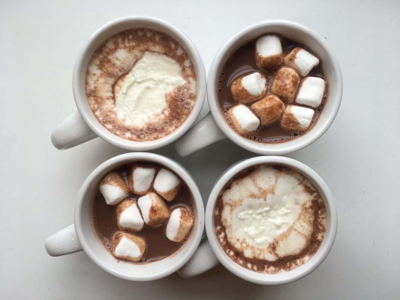 four cups of hot chocolate with marshmallows and whip cream