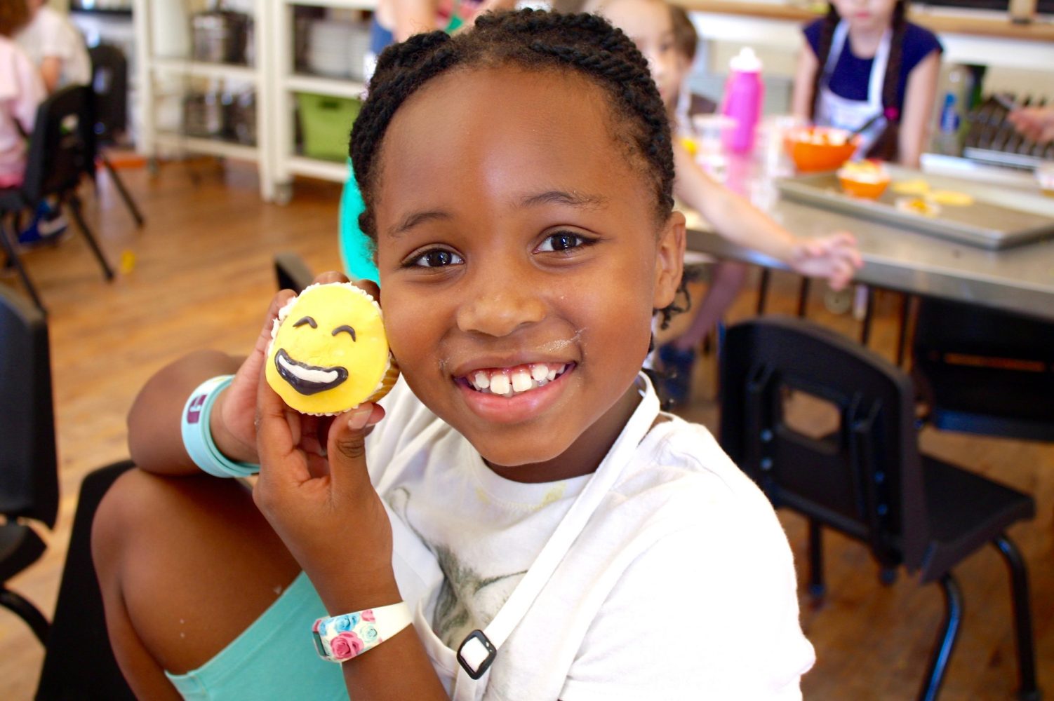 girl holding up a matching emoji smiling face cupcake