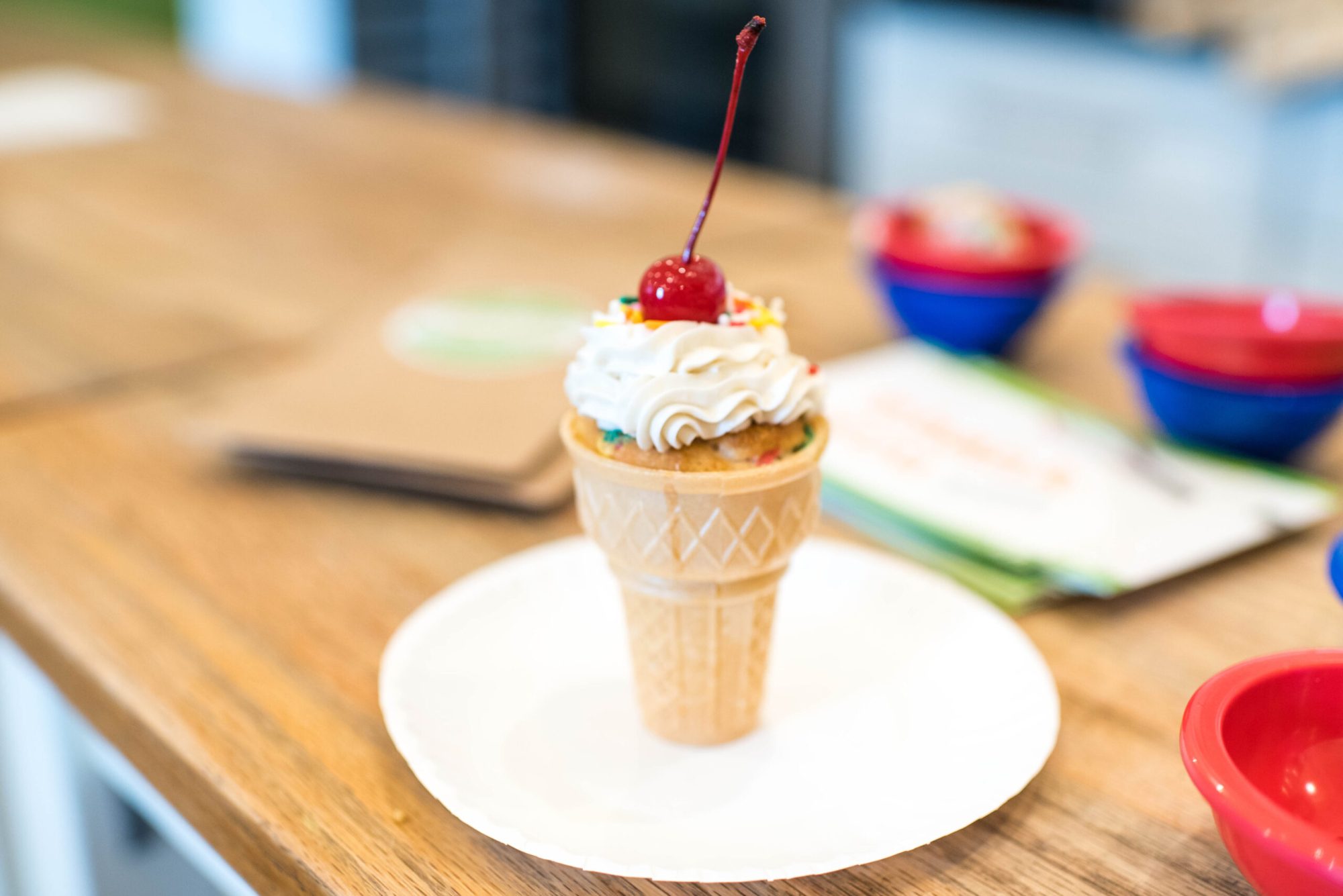 a cupcake in an ice cream cone with whip cream and a cherry on top