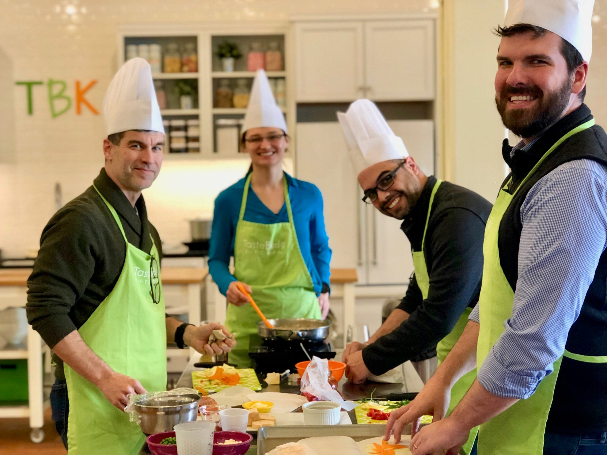 four adults standing in a kitchen preparing food