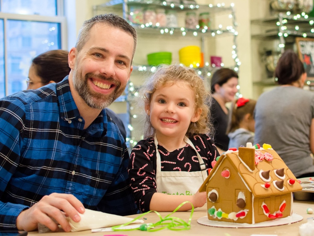 a father and daughter smiling in front of a gingerbread house