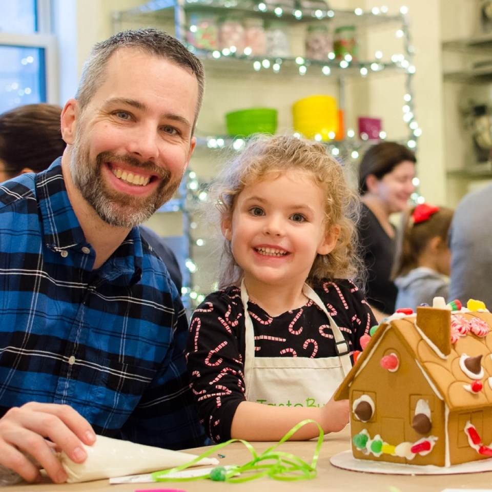 Family-GB9-1.jpg a father and daughter smiling in front of a gingerbread house