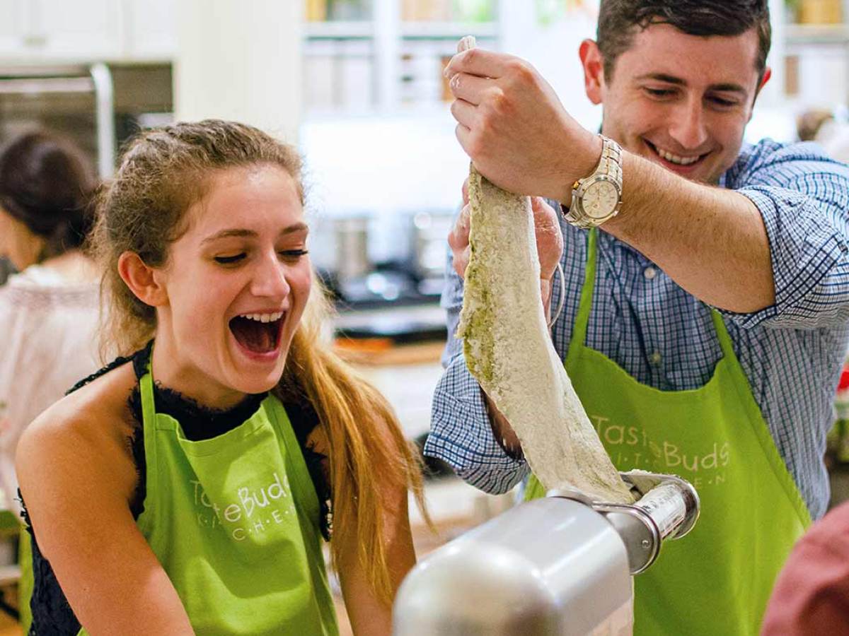 a couple serving homemade pasta dough into a cutting machine