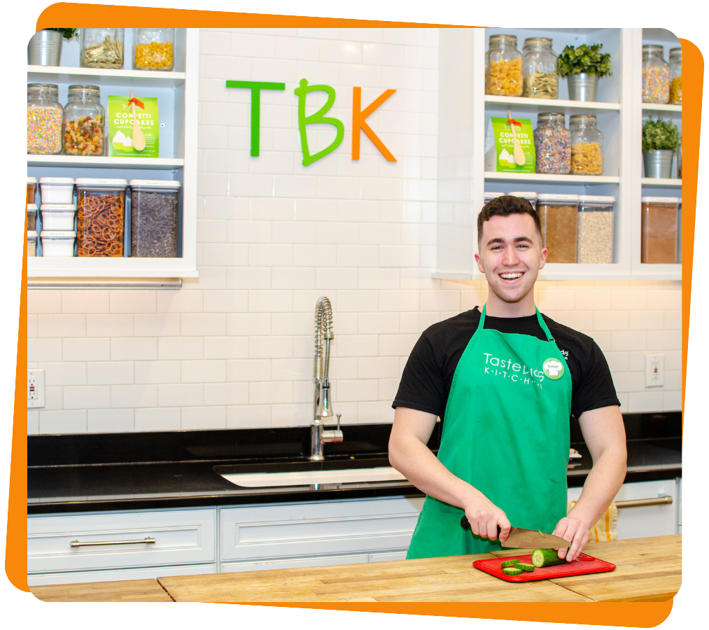 Untitled design (24) a man in an apron smiling in the kitchen using a cutting board