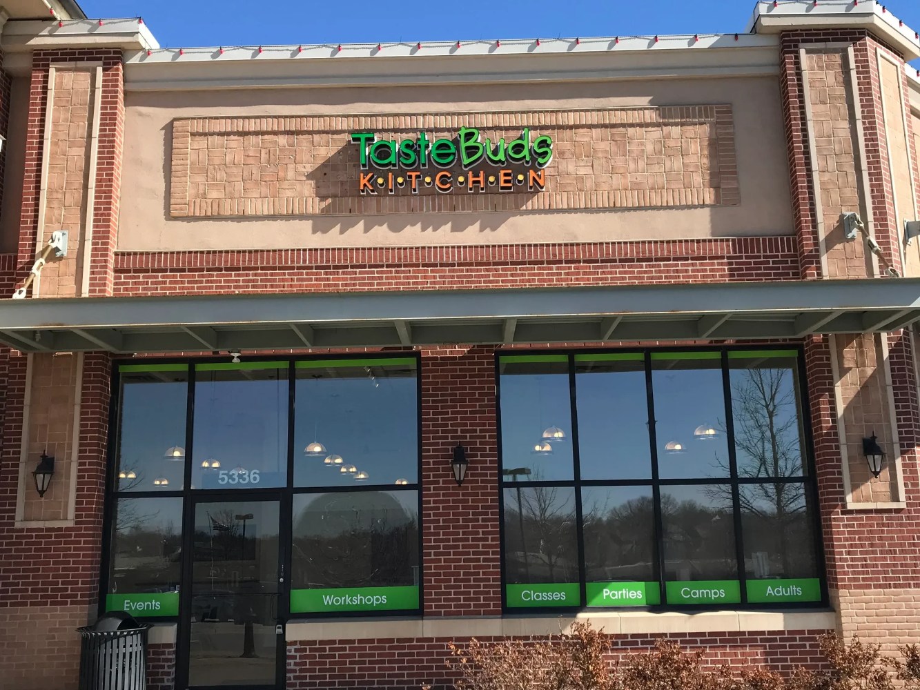 Storefront with 'Taste Buds Kitchen' sign, large windows, and green text listing activities.