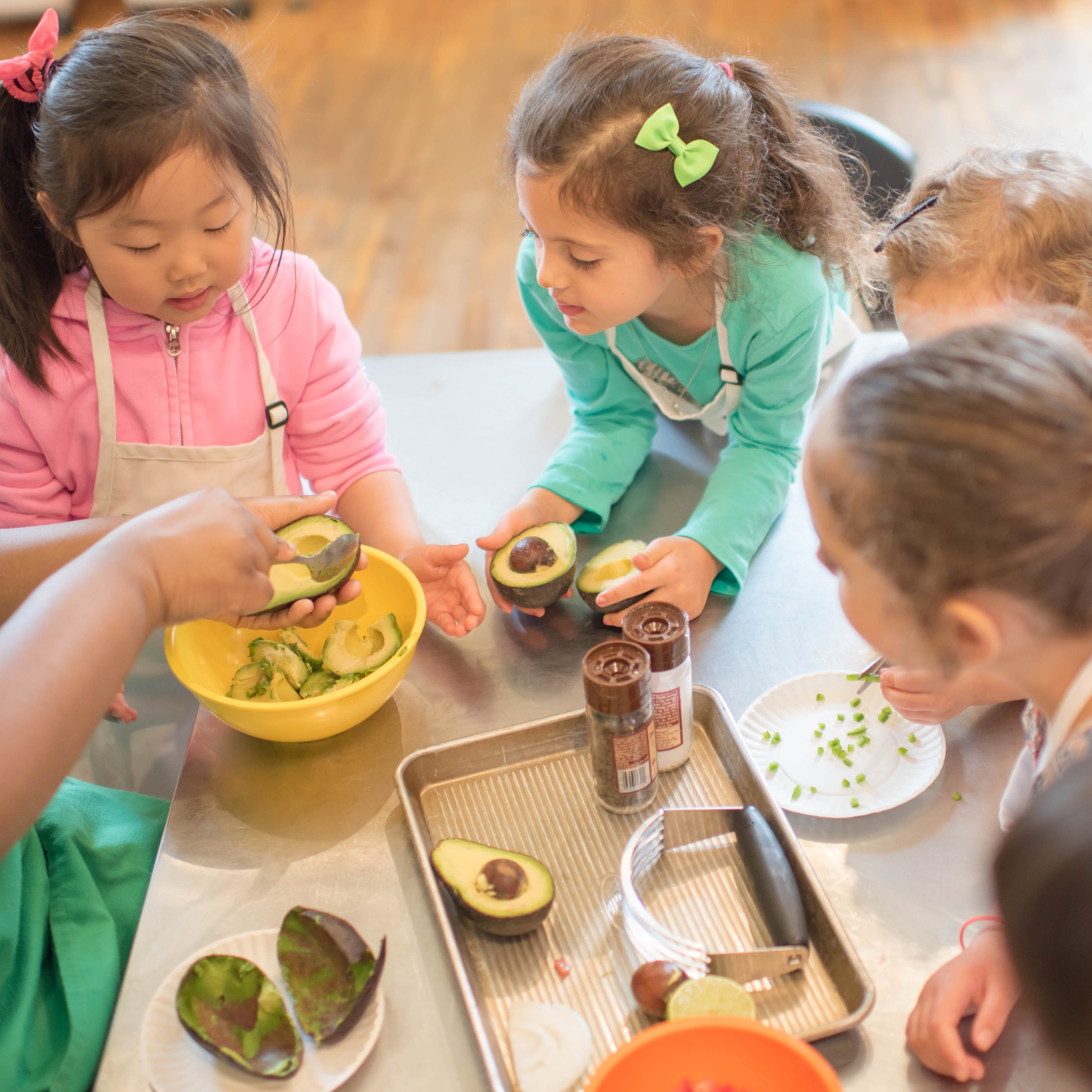 Children gathered around a table, learning to make guacamole with avocados.