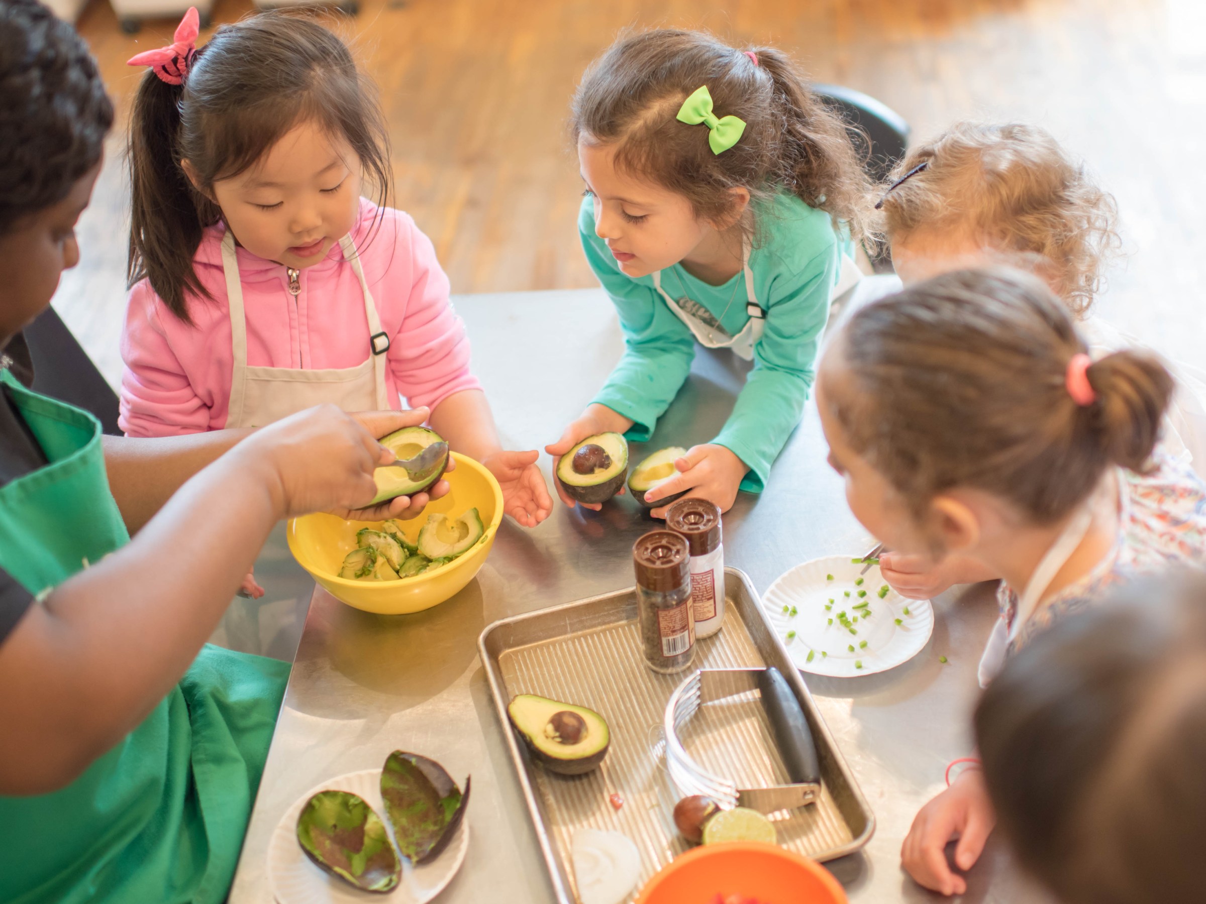 Children gathered around a table, learning to make guacamole with avocados.