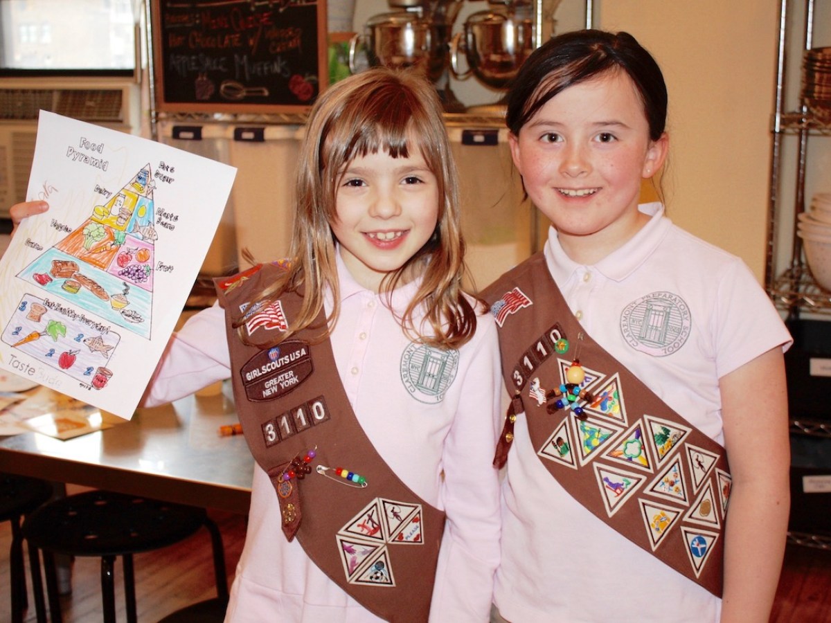 Two young Girl Scouts in uniforms, one holding a colorful food pyramid drawing.