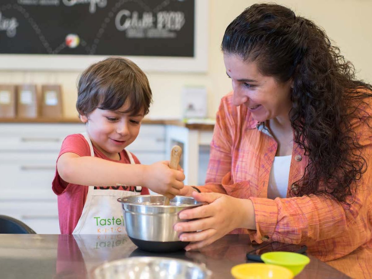 Woman and child smiling while mixing ingredients in kitchen bowl.