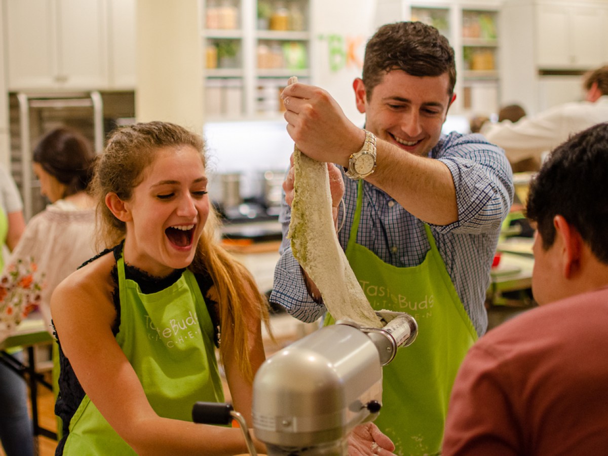 Group of people smiling and making dough in a kitchen.