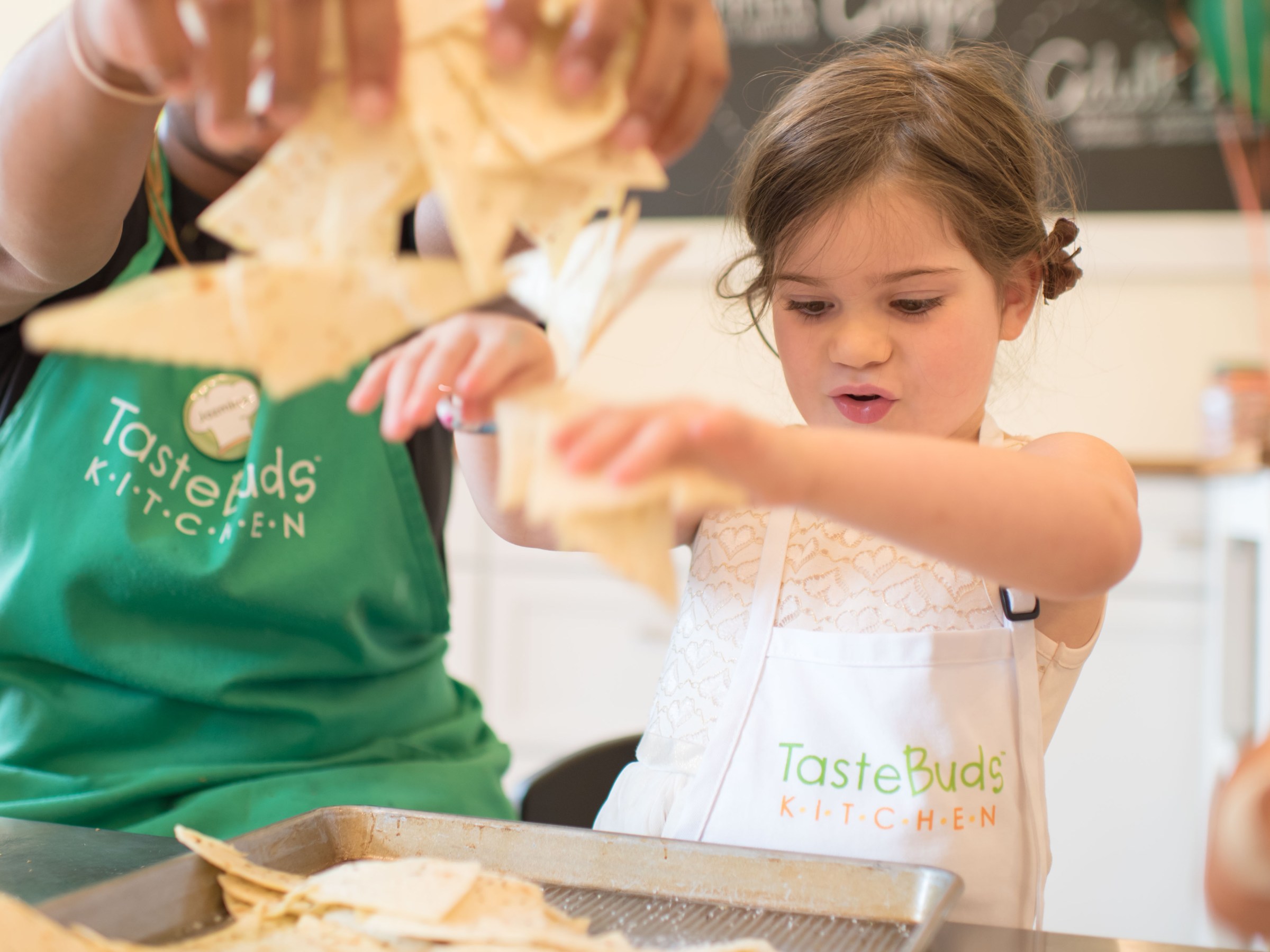 Child in an apron enthusiastically preparing food in a kitchen setting.